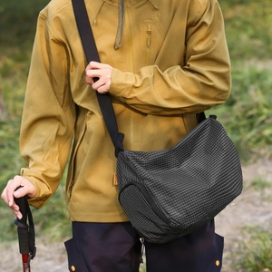 Détail d'un sac bandoulière en toile quadrillée avec étiquette orange sur la pelouse