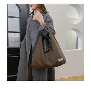 Close-up of the white logo label on the side of a brown canvas tote bag for women