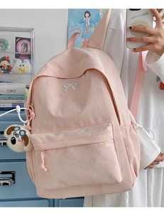 Detail of pink backpack featuring subtle bow patterns and a cute dog plush keychain charm