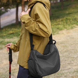 Détail du sac bandoulière noir à texture quadrillée avec étiquette orange en randonnée