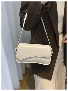 Detail of cream white leather baguette bag featuring an irregular curved flap design
