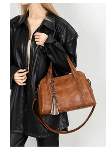 Brown leather handbag detail featuring a woven handle with a metallic tassel charm