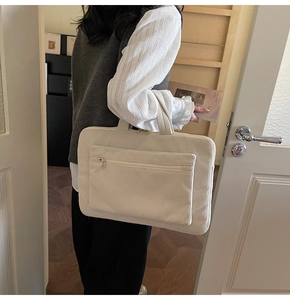Detail of a beige corduroy laptop bag with a front zipper pocket carried by a person