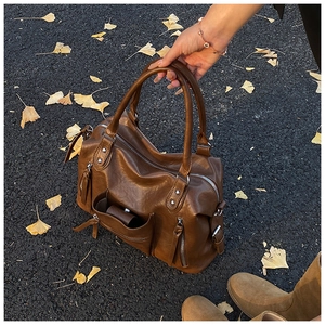 Detail view of a vintage brown PU leather commuter bag on an autumn ginkgo leaves background