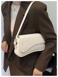 Detail of a minimalist white saddle bag with golden metal buckles on a brown blazer suit