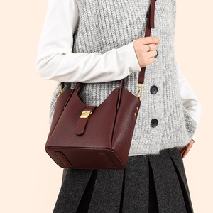 Détail du sac seau bordeaux en cuir avec fermoir doré porté par une femme mannequin