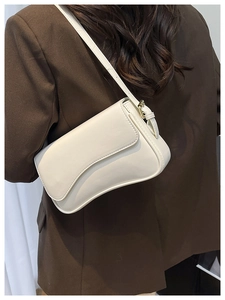 Detail of cream-colored shoulder bag with adjustable strap on a model in a brown blazer