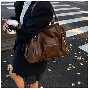 Detailed close-up of brown PU leather tote bag with exterior zippers and fringe tassels