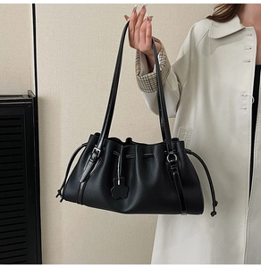 Detail of black tote bag with litchi texture, drawstring pleats, and bear charm pendant
