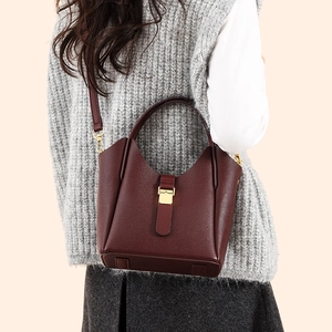 Détail d'un sac seau en cuir bordeaux avec boucle dorée porté par un mannequin