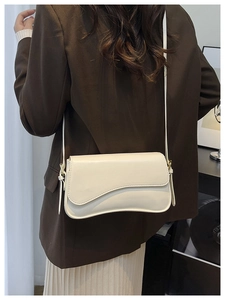 Detail of off-white leather shoulder bag featuring an asymmetrical wavy flap on a blazer
