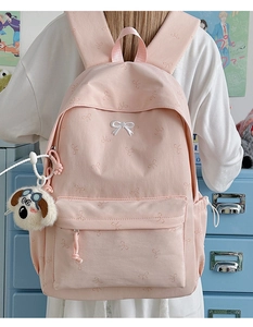 Close-up of pink canvas backpack featuring white bow embroidery and cute puppy plush pendant