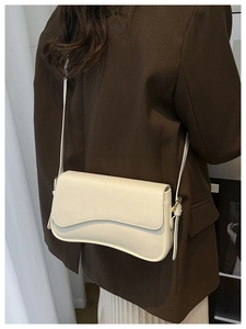 Detail view of the wave-shaped bottom design and adjustable strap on a cream PU leather bag