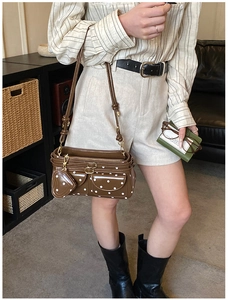Detail einer braunen gepunkteten Umhängetasche mit zwei Taschen und Herzanhänger