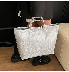 Detail of silver snake-embossed tote bag featuring white TOTE BAG text and metallic texture
