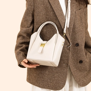 Détail du sac seau beige en cuir grainé avec boucle dorée porté par un mannequin