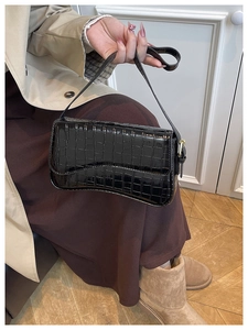 Detailed texture of black crocodile embossed patent leather on a stylish crescent bag
