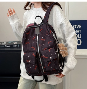 Détail d'un sac à dos noir avec nœuds rouges, pois blancs et un pendentif ours marron