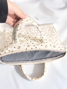 Close-up of beige corduroy shoulder bag with sweet heart and bow print and metal zipper