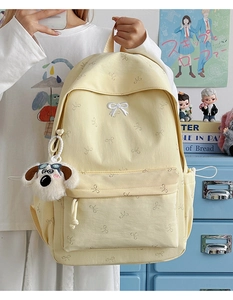 Detail of light yellow canvas backpack featuring white bow pattern and plush dog charm