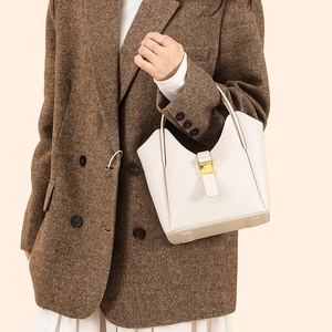 Détail d'un sac seau en cuir crème avec boucle dorée sur une veste en tweed brun