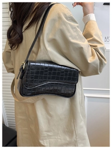 Detail of black crocodile pattern baguette bag with wave curved bottom on a model