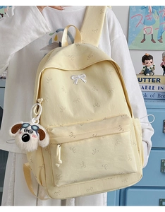Detail of cream yellow backpack featuring mini bow prints and a plush puppy pendant