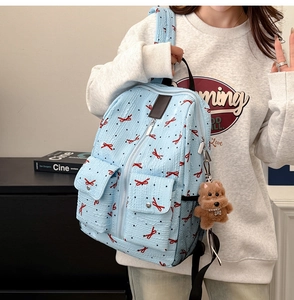 Détail d'un sac à dos bleu clair avec nœud rouge, pois noirs et breloque ours en peluche