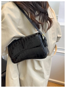 Detail of black crocodile pattern leather shoulder bag on trench coat with gold buckle