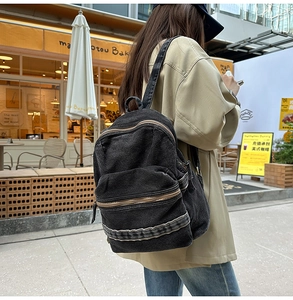 Vue de rue extérieure d'un sac à dos rétro en denim noir avec compartiments zippés
