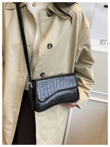 Detail of black crocodile texture glossy shoulder bag with golden metallic buckles