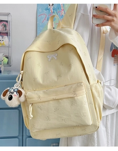 Close-up of a light yellow backpack with bow patterns and a white puppy plush pendant