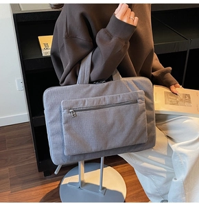 Grey corduroy laptop bag with a front zipper pocket held by a model in casual wear