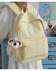 Close-up of yellow canvas backpack with bow embroidery and cute dog plush keychain