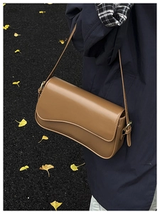 Brown leather shoulder bag with wave edge flap detail and gold buckle in autumn setting