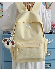 Detail view of cream canvas backpack featuring bow embroidery and cute plush dog charm