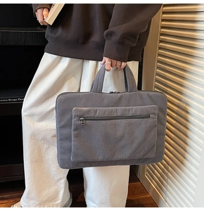 Close-up of a gray corduroy laptop bag featuring a large front pocket and durable handles