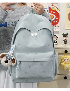 Close-up of light blue backpack featuring bow print and plush dog charm detail