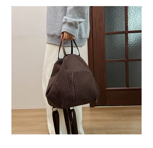 Close-up of brown plaid canvas backpack with handle and zipper pocket detail