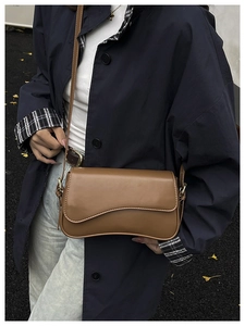 Close-up of brown vintage leather crossbody bag with wave curve flap and gold buckle