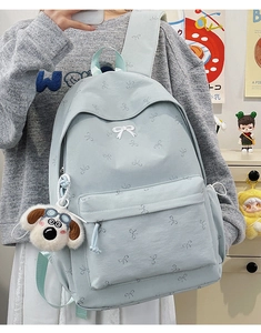 Close-up of light blue backpack with white bow prints and a plush dog charm on mirror