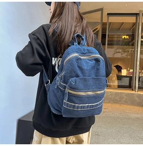 Détail d'un grand sac à dos en jean bleu foncé avec texture délavée porté par une personne