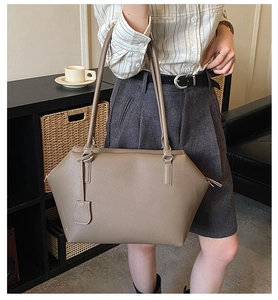 Detail view of a large taupe pebbled leather tote bag being carried by a model
