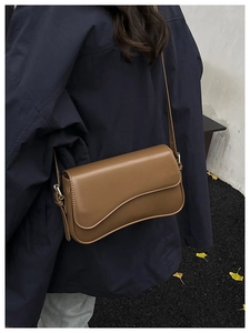 Detail view of brown leather crossbody bag with unique wavy flap and fine stitching details