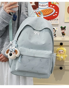 Detail of light blue backpack with white bow patterns and plush dog charm pendant