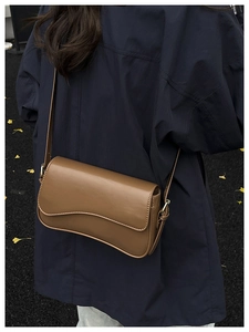 Detail view of brown shoulder bag with wavy flap design shown on model in autumn setting