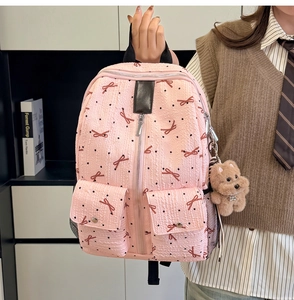 Détail d'un sac à dos rose avec broderies de nœuds rouges, doubles poches et ours en peluche