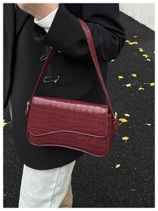 Close-up of a burgundy croc-effect underarm bag with a gold buckle on the shoulder strap
