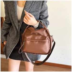 Detail of a brown nylon crossbody bag with sturdy handles and adjustable strap on a model