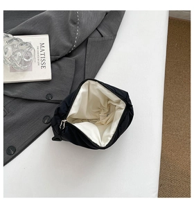 Detailed view of black quilted makeup bag with zipper and white lining on grey suit